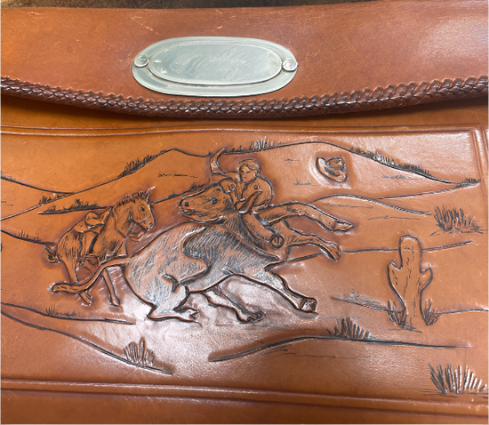 Brown leather bag with embossed design of a rider on horseback and landscape.